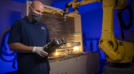 Komico Technology employee working in factory with heavy machinery.